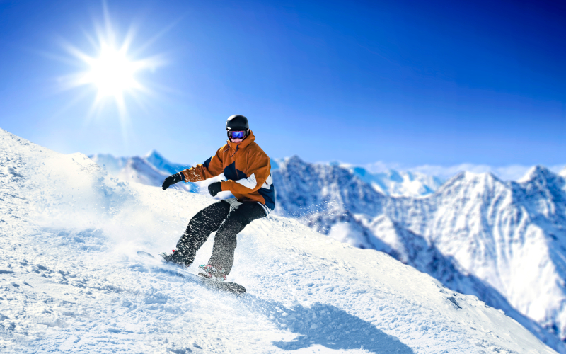 Un snowboarder dévalant les pistes de ski sous un beau soleil