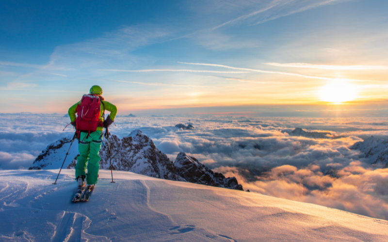 Un skieur de dos admirant un coucher de soleil sur les montagnes dans les Alpes du Sud