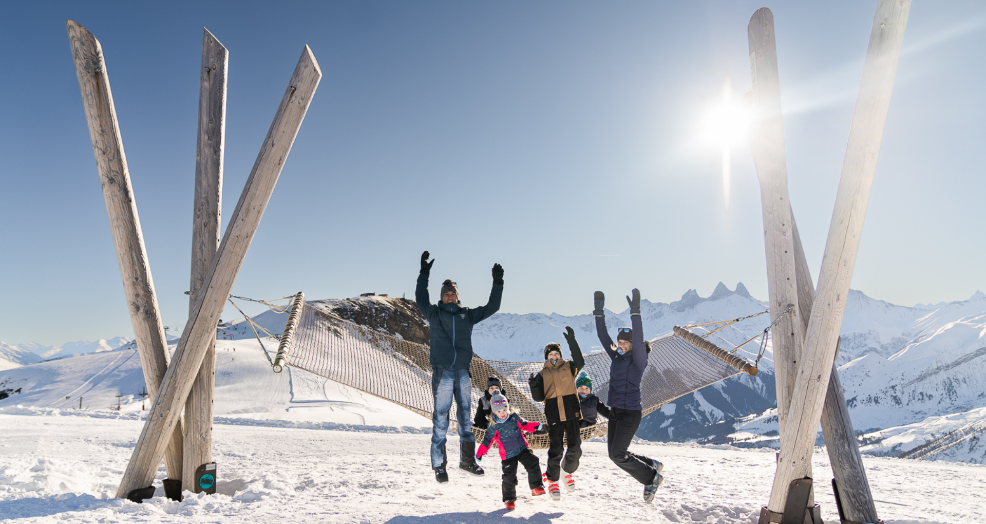 Une famille au ski sautant dans les airs devant le hamac des Sybelles
