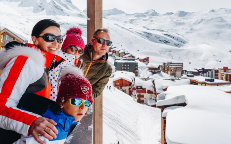 Une famille sur un balcon admirant la vue sur les montagnes enneigées de Val Thorens
